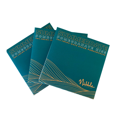 Three square Nibble London Summer Date Pomegranate Kiss chocolate bars in teal packaging with gold text and wave details, arranged on a white background.